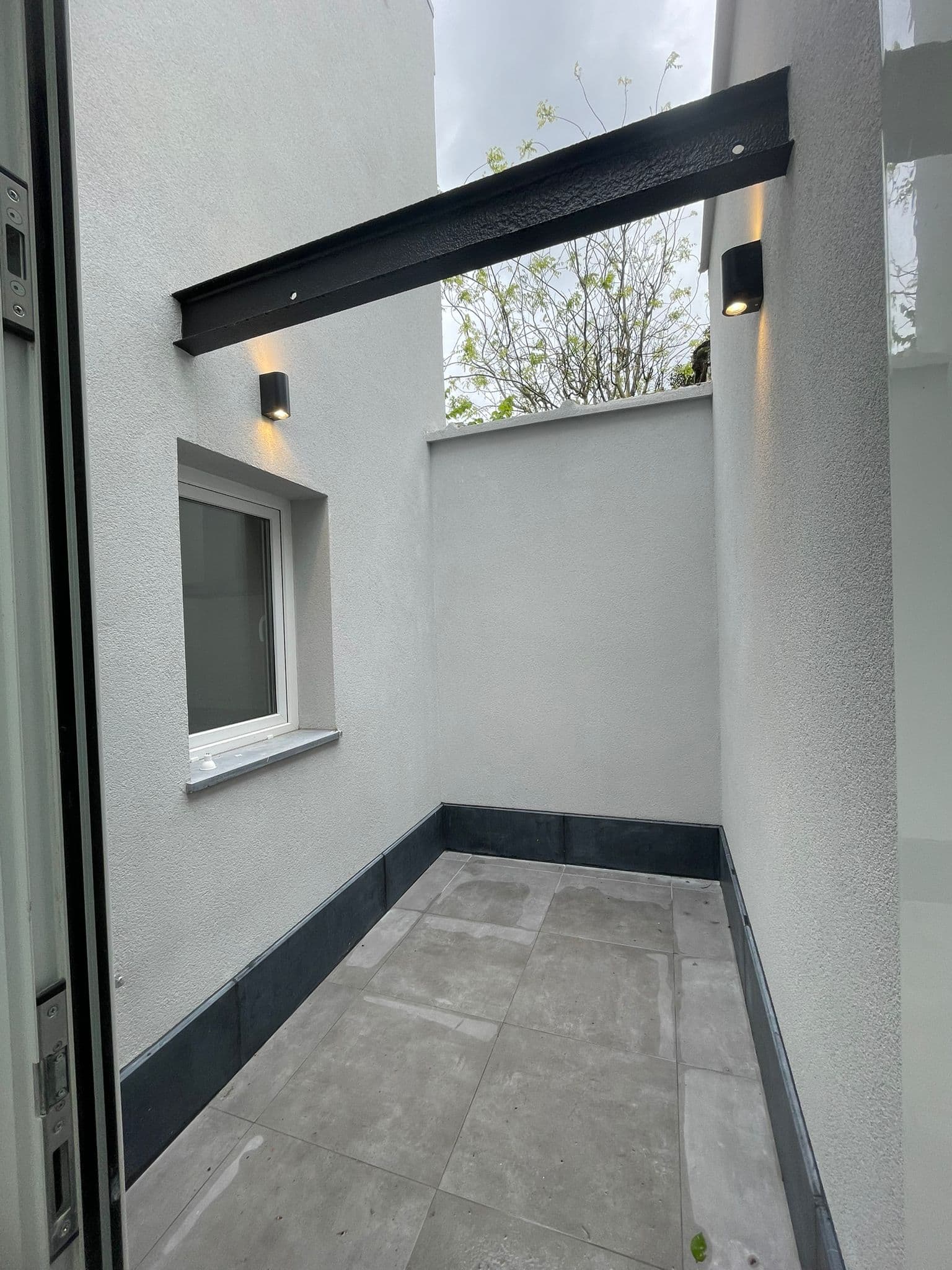 Binnentuin na renovatie — witte crepi muren, tegels en sfeerverlichting
