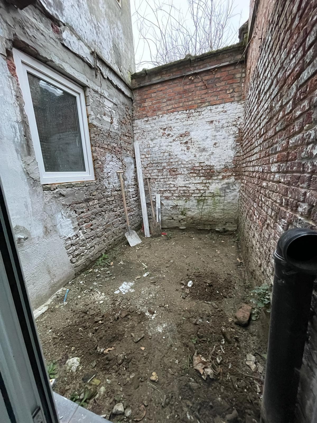 Binnentuin vóór renovatie — kale bakstenen muren en onbevloerd